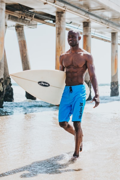 白天，男人拿着冲浪板在海边散步